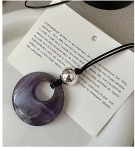 Macro detail of natural purple stone pendant with silver bead on a black cord necklace