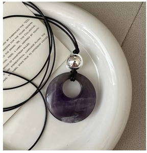 Detail of a purple amethyst donut pendant with a silver bead on a black woven cord