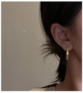 Close-up of minimalist gold drop earrings with polished finish on model's ear