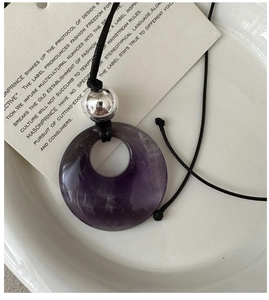 Macro shot of a purple natural stone circular pendant with a polished silver orb on black cord