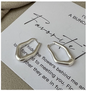 Macro detail of matte silver geometric wavy hoop earrings on a textured background