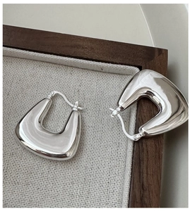 Macro detail of polished 925 sterling silver U-shaped hoop earrings on linen