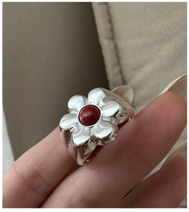 Macro shot of a floral S925 silver ring with a red gemstone on a finger