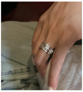 Macro shot of silver wide ring with irregular wave texture worn on hand over denim