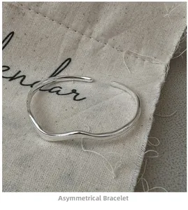 Close-up of irregular wave silver bracelet with polished finish on a linen bag