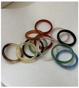 Gros plan d'un lot de 12 bagues colorées en résine aux tons variés sur fond beige