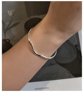 Macro shot of minimalist wavy silver open bangle showing sleek polished metal texture