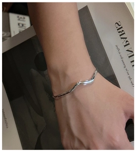 Macro shot of minimalist silver wavy bangle with polished texture and fluid design