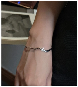 Close-up of minimalist wave-patterned sterling silver bracelet on female wrist