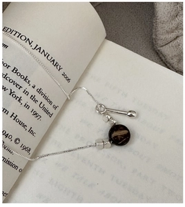 Detailed view of silver box chain necklace with black pendant on vintage book pages