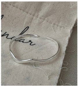 Detail of wavy S925 silver open bangle displayed on a rustic beige linen pouch