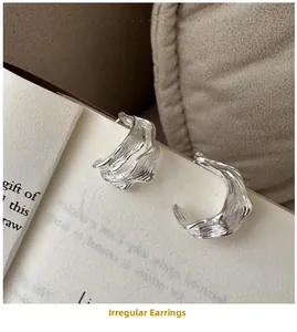 Macro detail of silver S925 earrings with textured curved design on a white book page