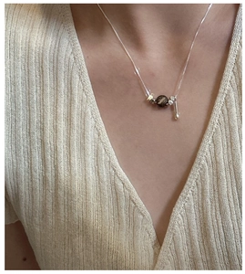 Detail of S925 sterling silver chain necklace with brown textured bead on beige knitwear