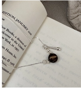 Detail of silver chain necklace with retro round pendant and T-bar toggle clasp on book