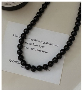 Macro shot of glossy black beaded silver necklace on white card with decorative bottle
