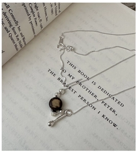 Detailed view of S925 silver water drop necklace with dark brown bead on a book