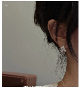 Detail view of silver earrings with irregular textured surface worn on the ear