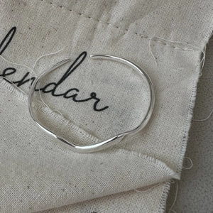 Minimalist S925 sterling silver wavy open bangle with polished surface on linen background