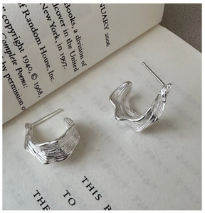 Detailed macro view of S925 silver hoop earrings with irregular lava texture on an open book
