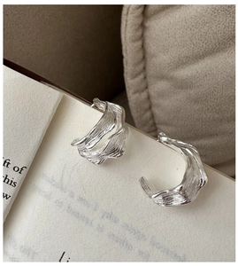 Detail shot of silver S925 earrings with irregular pleated texture on book surface