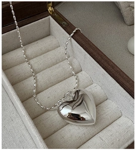Gros plan d'un grand pendentif cœur en argent poli sur une chaîne à perles dans un coffret
