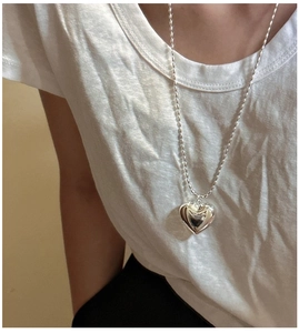 Gros plan d'un long collier à perles argentées avec pendentif cœur sur un t-shirt blanc