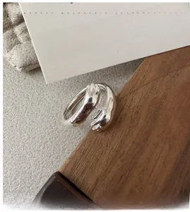 Dettaglio dell'anello abbraccio in argento S925 con mani lucide su supporto di legno