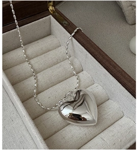 Détail d'un pendentif coeur en argent poli sur une chaîne à billes dans un écrin à bijoux
