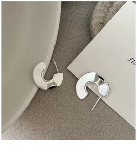 Detail of matte silver C-shaped earrings with irregular textured finish in a minimal style