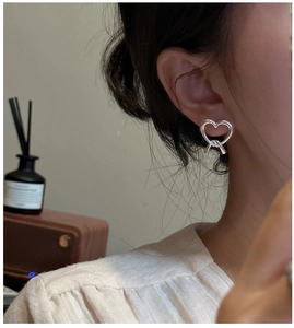 Close-up of matte silver heart-shaped knot stud earring worn by a model in soft light