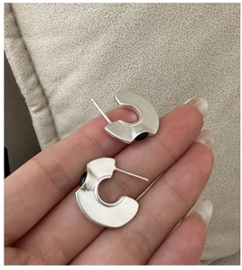 Close-up of C-shaped silver earrings with matte texture and black onyx circular inlay