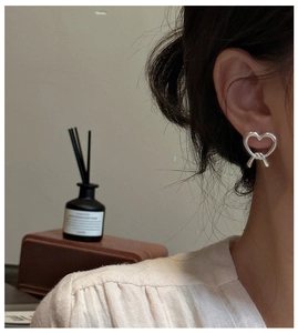 Detail of silver matte heart earring with unique twist knot on model's ear