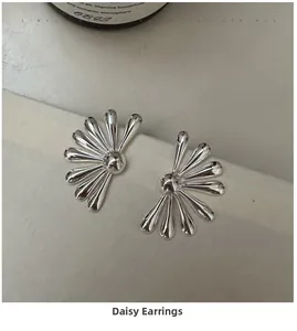 Macro view of polished silver daisy earrings on minimalist stone surface background