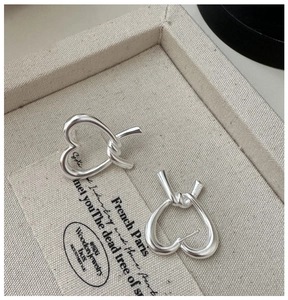 Macro detail of silver S925 heart knot earrings resting in a textured jewelry box