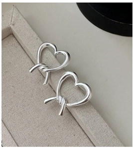 Detailed close-up of matte silver heart earrings with a unique twisted knot design on linen