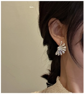 Macro shot of silver fan-shaped stud earrings on a model showing polished finish