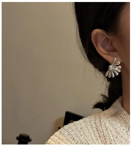 Close-up of elegant silver fan-shaped earrings worn by a model in warm natural light