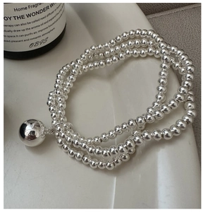 Macro shot of silver triple-layered beaded bracelet with a large polished metal sphere pendant