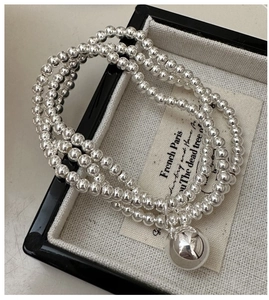 Detail of triple-layer silver beaded bracelet featuring a polished mirror-finish round charm