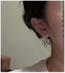 Gros plan de boucles d'oreilles fleurs en argent S925 portées sur un fond beige neutre
