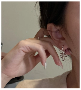 Gros plan d'une boucle d'oreille fleur en argent minimaliste et d'une bague sur un mannequin