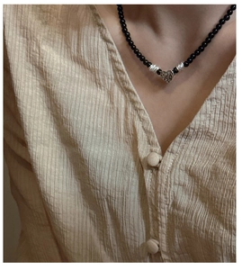 Détail d'un collier de perles noires avec un pendentif cœur argenté texturé porté
