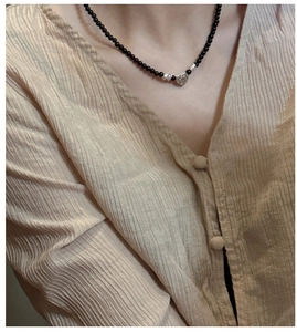 Gros plan d'un collier de perles noires avec pendentif cœur en argent texturé sur modèle