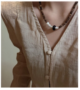 Détail d'un collier en argent S925 avec perles œil de tigre sur un mannequin en lin