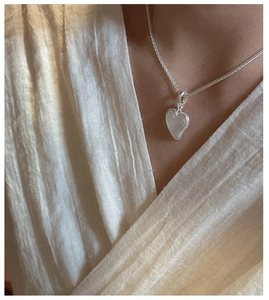 Détail macro d'un pendentif cœur en argent avec incrustation blanche sur chaîne épi