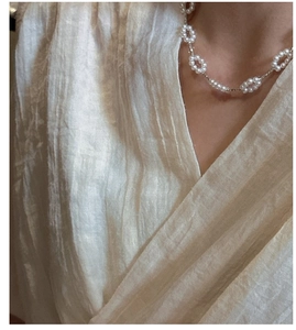 Detail of silver chain necklace with small white pearl flower clusters on textured fabric