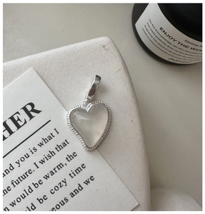Gros plan d'un pendentif cœur en argent S925 avec agate blanche et bord perlé sur pierre