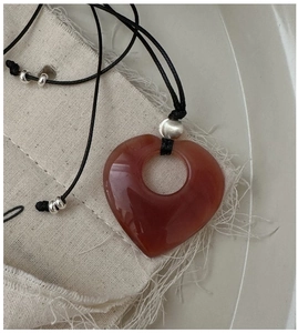 Dettaglio di un ciondolo a cuore in corniola su un cordoncino nero di cuoio