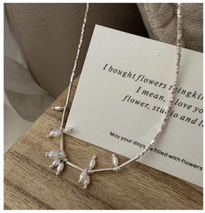 Macro shot of silver chain with irregular pearls and metal tubes on wood base