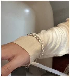 Detail of layered S925 sterling silver beaded bracelet on a wrist with knitwear